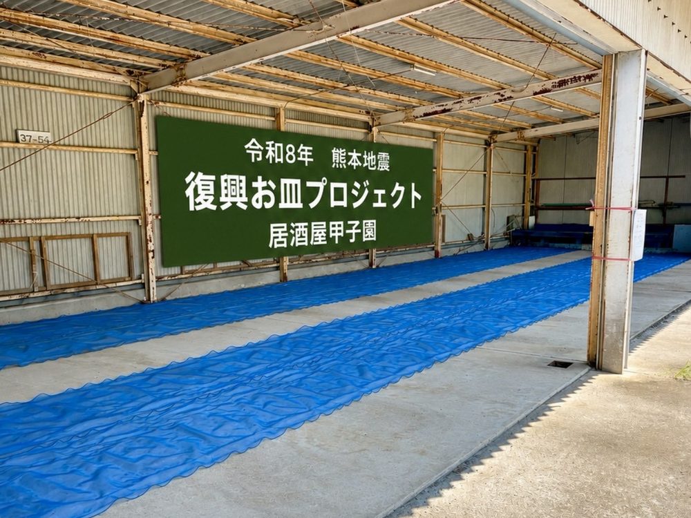 受入場所の倉庫。「令和8年 熊本地震 復興お皿プロジェクト 居酒屋甲子園」と書かれた看板の前に、ブルーシートが敷かれている
